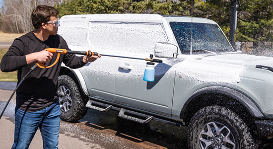 A person applies AMSOIL High-Foam Car Shampoo to a vehicle.