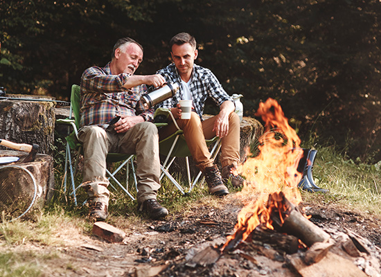 Two men enjoy coffee by the fire.
