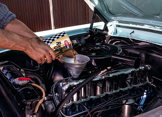 An early iteration of AMSOIL motor oil is poured into a classic Ford Mustang.