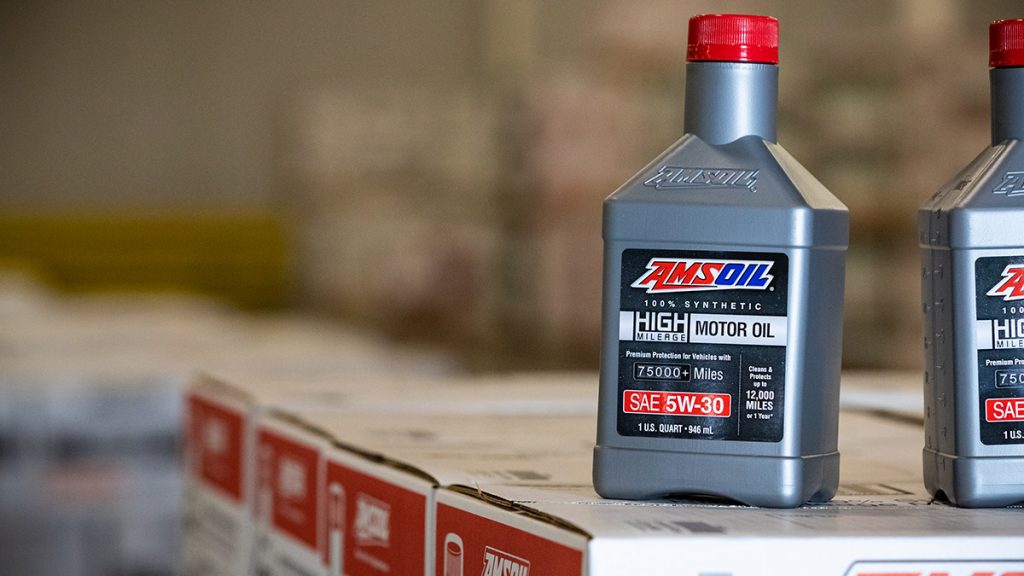 Quart-sized container of AMSOIL High-Mileage 100% Synthetic Motor Oil sits on a stack of cases.