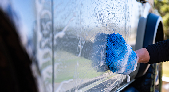 A person uses a car-shampoo micro-fiber mitten to wash their vehicle.