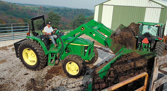 Farm tractor loads manure onto a manure spreader.