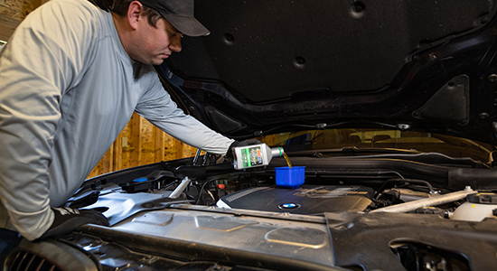 A man pours motor oil into his vehicle while performing an oil change.