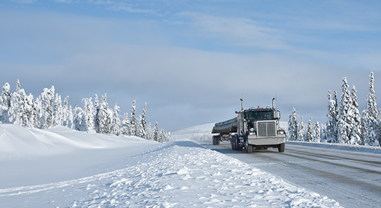 Semitruck pulls a heavy load over a snowy mountain road.