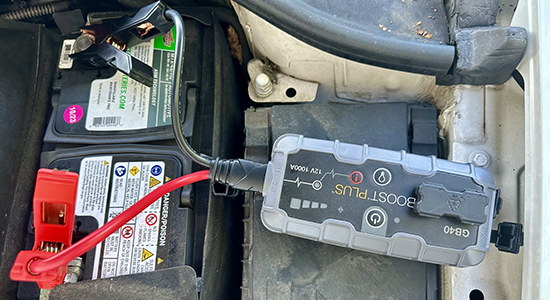 A portable jump starter is hooked up to a car battery.