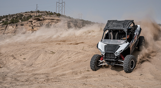 A UTV throws up dust on a banked turn.