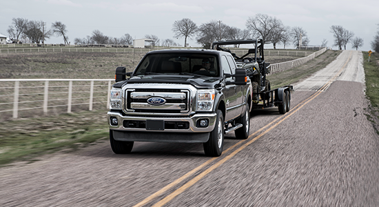 A pickup truck pulls an UTV down a rural road.