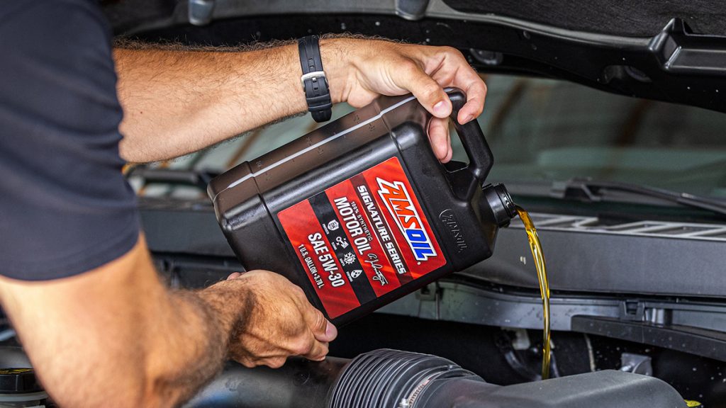 Pouring AMSOIL Signature Series 100% Synthetic Motor Oil from a gallon into a Ford F-150 Raptor engine