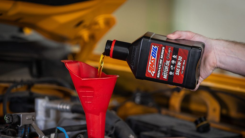 Pouring AMSOIL Signature Series 100% Synthetic Motor Oil from a quart through a red funnel