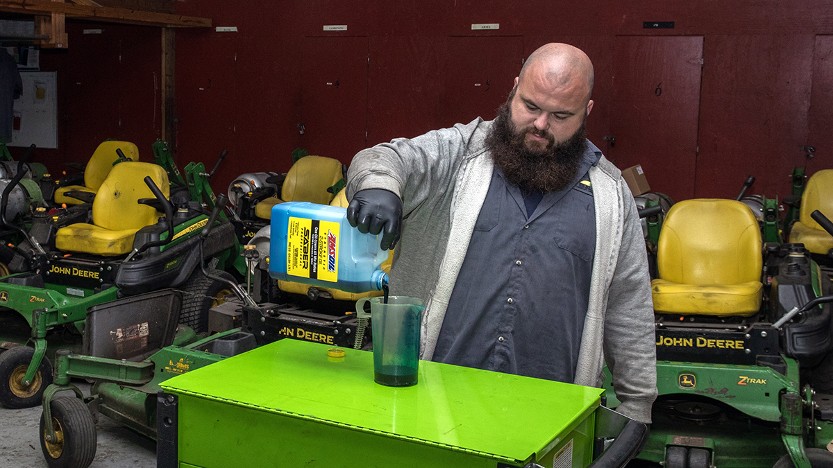 A B&M Landscape Concepts technician pours AMSOIL SABER 2-stroke oil