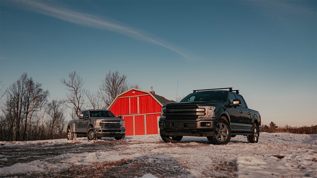 Two pickup trucks parked in the snow in front of a red barn
